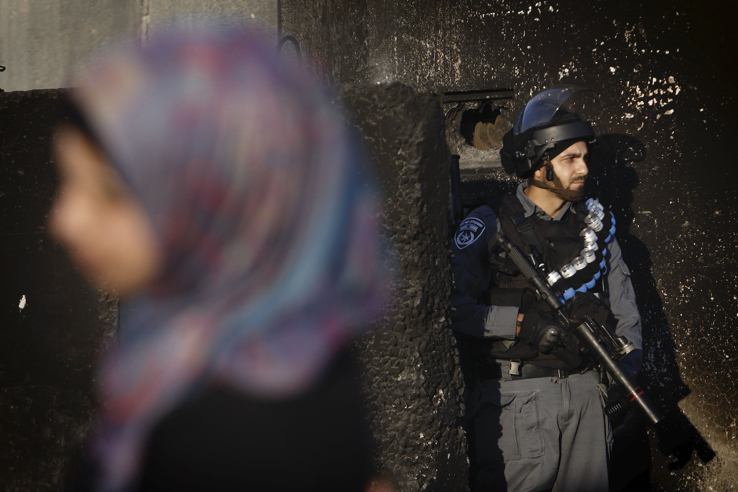 An Israeli soldier stands guard at the Qalandiya checkpoint on the outskirts of the West Bank city of Ramallah as a Palestinian woman waits to cross the checkpoint to head to Jerusalem, July 04, 2014. (Miriam Alster/Flash90)