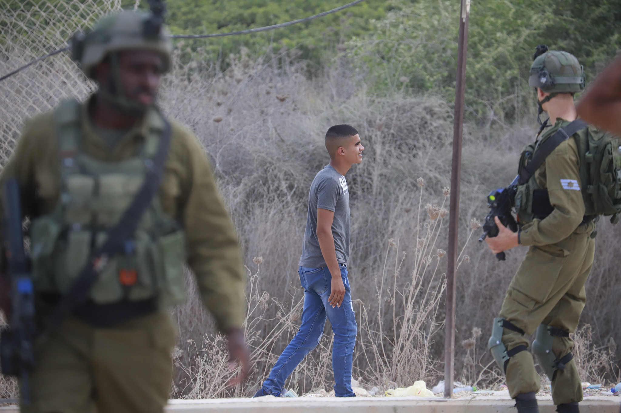 A Palestinian walks by Israeli soldiers close to a hole in the Israeli separation barrier next to the West Bank village of Far’oun near Tulkarem. (Activestills)