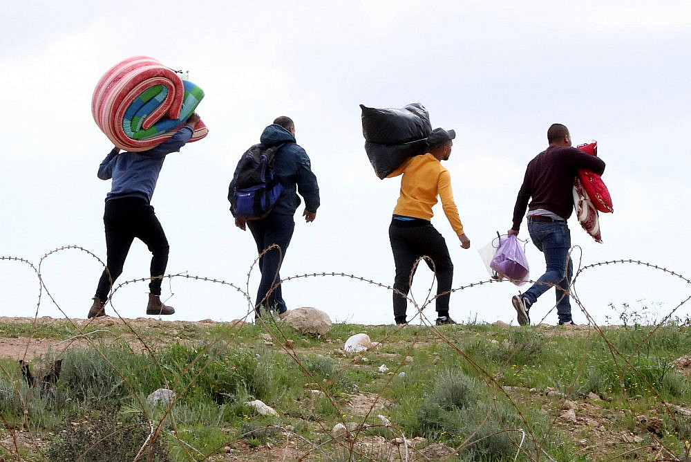 Palestinian workers from Hebron carry personal belongings as they cross through a hole in the Israeli security fence, after entrance into Israel was banned following the spread of the coronavirus, near the West Bank city of Hebron, March 22, 2020. (Wisam Hashlamoun/Flash90)