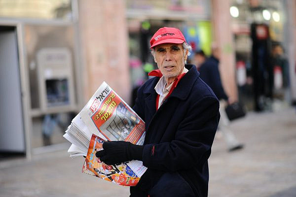 A man passes out the free daily newspaper Israel HaYom to passersby on Ben Yehuda Street in Jerusalem on February 6, 2015. (Mendy Hechtman/Flash90)