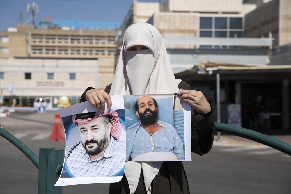 Taghrid al-Akhras, wife of Palestinian administrative detainee Maher al-Akhras, holds up photographs of her husband outside Kaplan Medical Center in Rehovot, where he is on day 73 of a hunger strike. (Oren Ziv/Activestills)