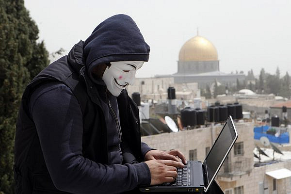 A Palestinian youth wearing a mask used by computer hackers who attacked a number of Israeli websites, seen backdropped by the Dome of the Rock, in Jerusalem's Old City. April 8 2013. (Sliman Khader/Flash90)