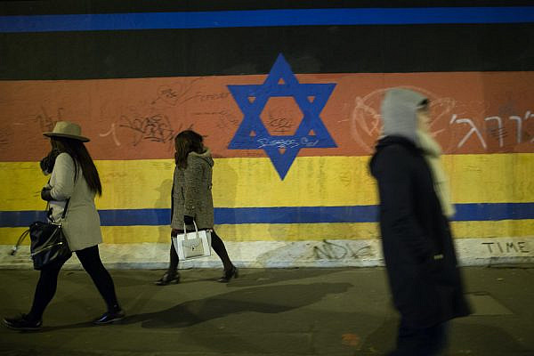 People walk by a mural depicting a combination of the Israeli and German flags on the Berlin Wall, March 13 , 2016. (Noam Revkin Fenton/Flash90)