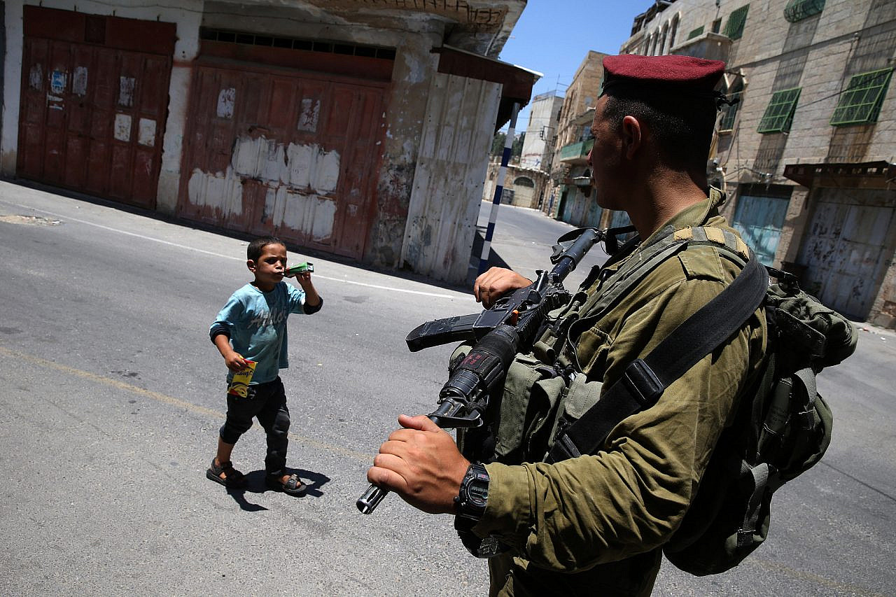 A Palestinian boy walks near Israeli soldiers in the Old City of Hebron, occupied West Bank, July 4, 2014. (Nati Shohat/Flash90)