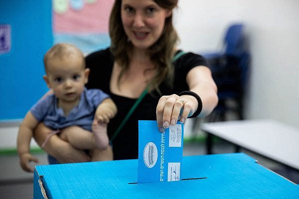A woman holds her baby as she casts her ballot for Knesset elections at a voting station in Jerusalem, on September 17, 2019. (Yonatan Sindel/Flash90)