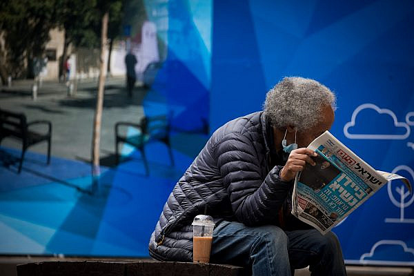 A man wears a face mask and reads newspaper in downtown Jerusalem on Nov. 8, 2020. (Yonatan Sindel/Flash90)