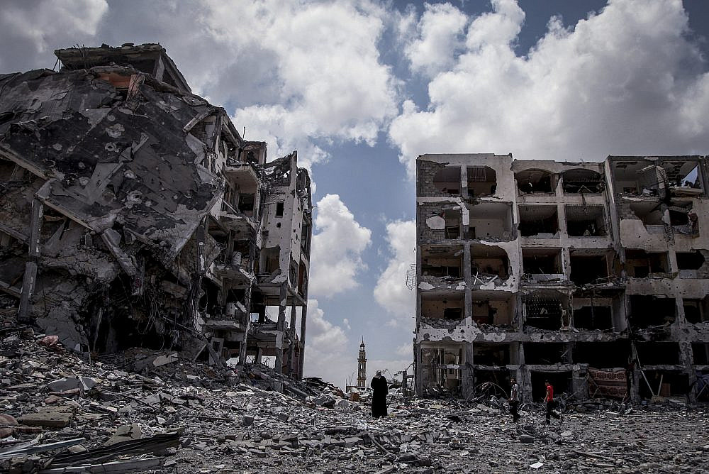 Palestinians walk in front of buildings destroyed by Israeli military forces in the northern Gaza Strip town of Beit Lahiya, Aug. 4, 2014. (Emad Nasser/Flash90)