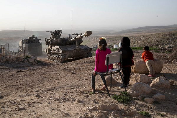 Children in Jinbeh, a Palestinian village in the occupied West Bank, watch as the Israeli army conducts a drill, February 3, 2020. (Keren Manor/Activestill.org)