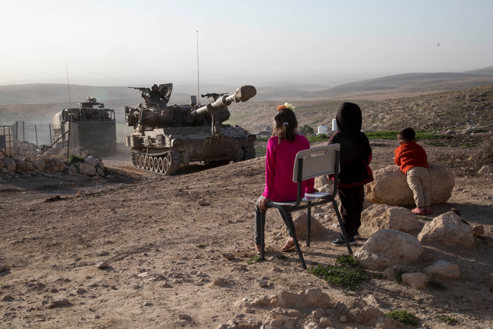 Children in Jinbeh, a Palestinian village in the occupied West Bank, watch as the Israeli army conducts a drill, February 3, 2020. (Keren Manor/Activestill.org)