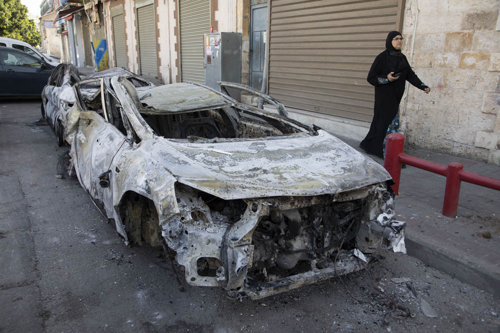A Palestinian woman walks by a burned out car in the city of Lydd in central Israel, following a night of violence between Jews and Palestinians in the city, May 12, 2021. (Oren Ziv)