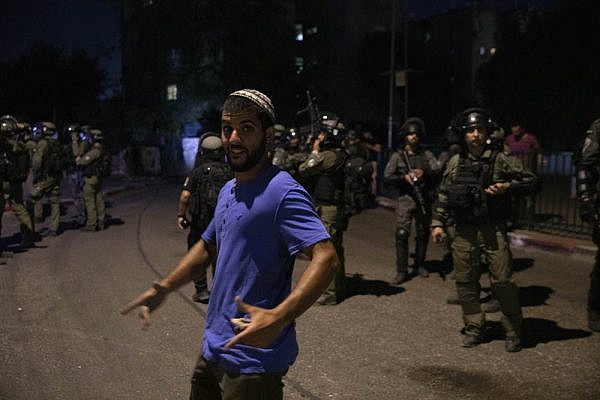 A right-wing Israeli seen standing in front of Israeli Border Police officers during attacks by security forces, rightists, and settlers on Palestinians in the city of Lyd, central Israel, May 13, 2021. (Oren Ziv)