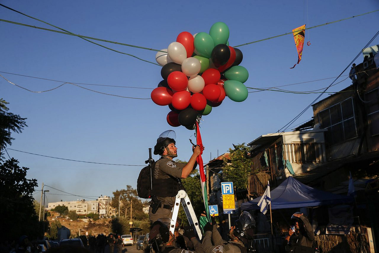 An Israeli police officer tries to take down balloons released by Palestinians in the East Jerusalem neighborhood of Sheikh Jarrah on May 15, 2021. (Jamal Awad/Flash90)