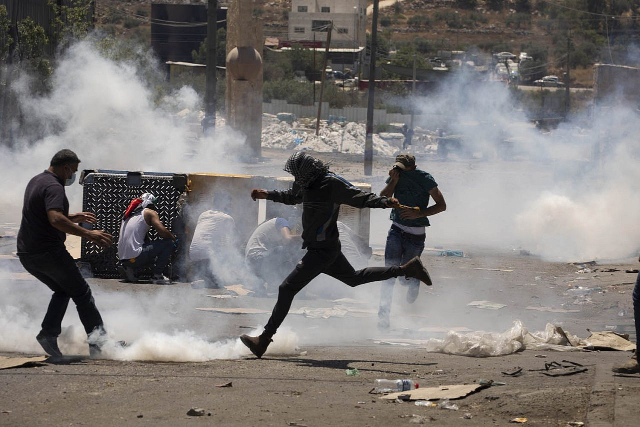 Palestinians throw stones and dodge tear gas shot by Israeli soldiers in the West Bank town of Beita, during a protest against the settlement outpost of Eviatar, June 18, 2021. (Oren Ziv)