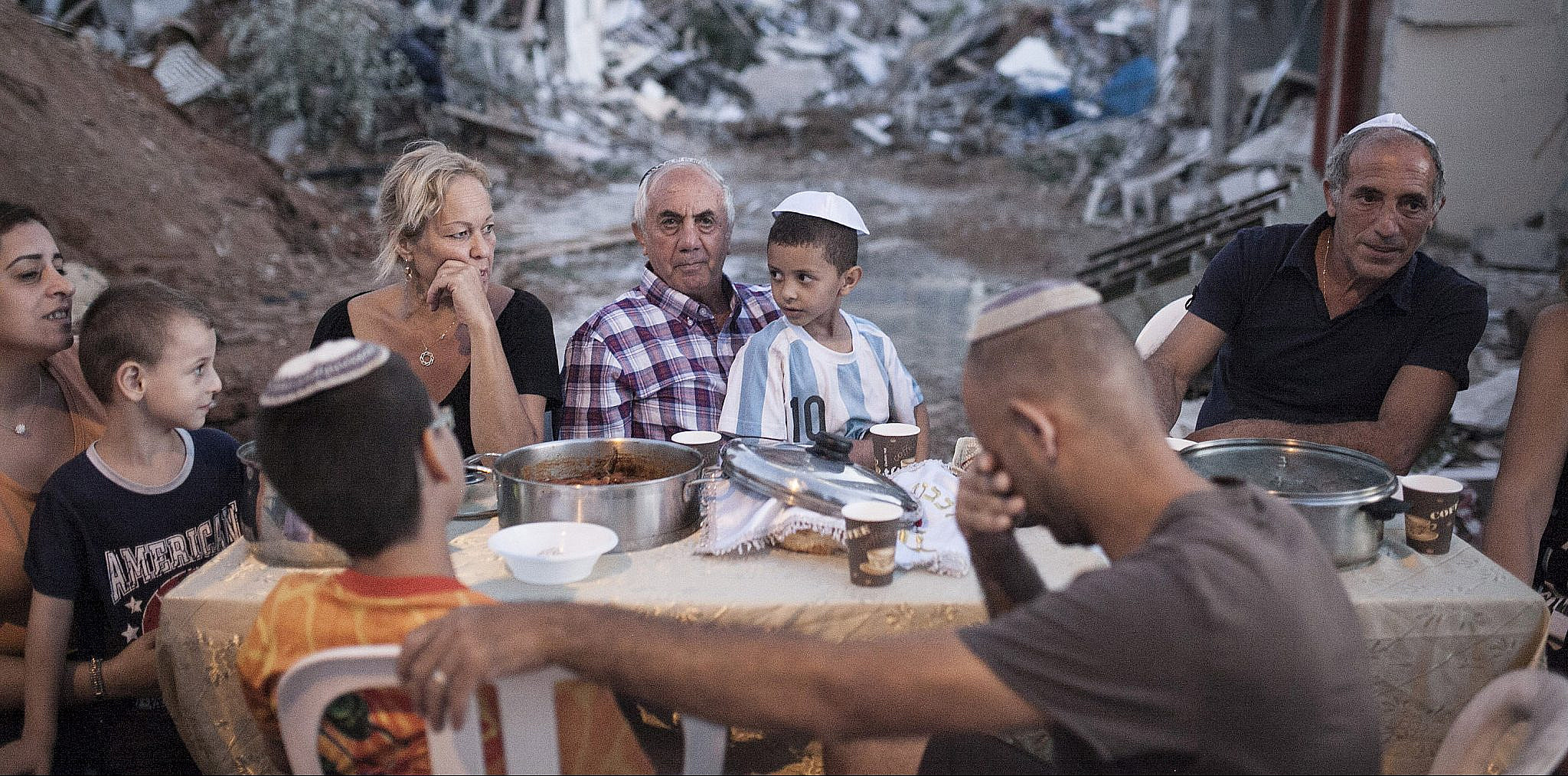 Three families hold an improvised, outdoor Shabbat dinner in the Tel Aviv neighborhood of Givat Amal. Their homes were demolished following a years-long struggle against eviction without proper compensation, September 19, 2014. (Shiraz Grinbaum/Activestills.org)