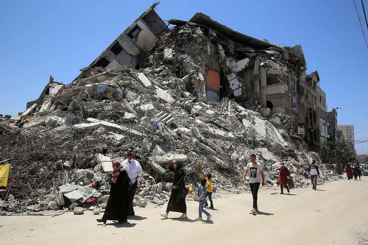 Palestinians walk next to a destroyed house in Rafah, after it was hit by Israeli air strikes during Operation Guardian of the Walls, in the Al-Rimal neighbourhood in Gaza City, May 30, 2021. (Abed Rahim Khatib/Flash90)