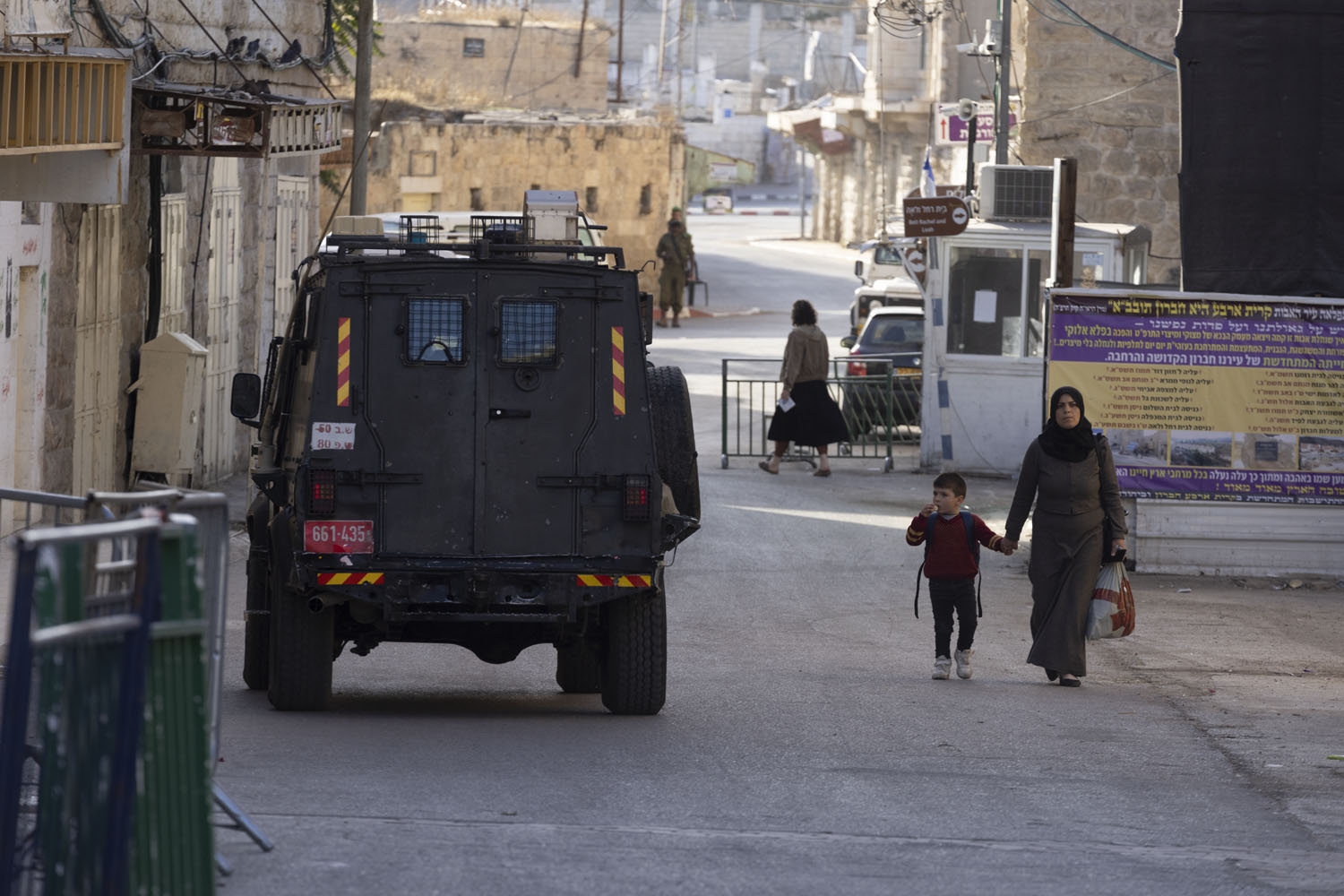 Palestinian mother and child walking next to an Israeli military jeep in Hebron, West Bank, Nov. 28, 2021. (Oren Ziv)