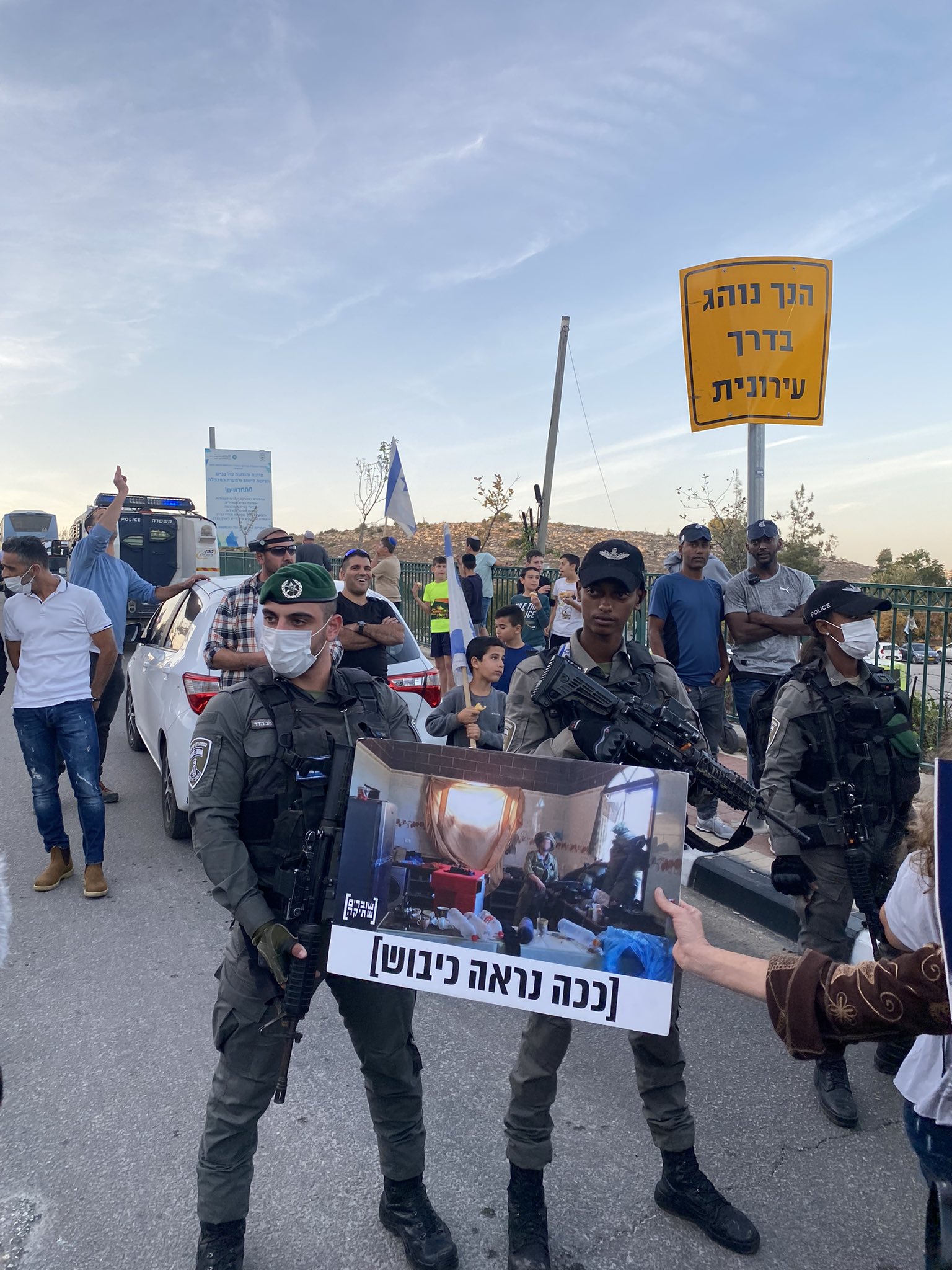 Un manifestante mette un cartello davanti ai soldati israeliani con la scritta "Ecco come appare l'occupazione", durante una manifestazione contro la visita del presidente Isaac Herzog a una cerimonia di Hanukkah a Hebron, 28 novembre 2021. (Ben Reiff)