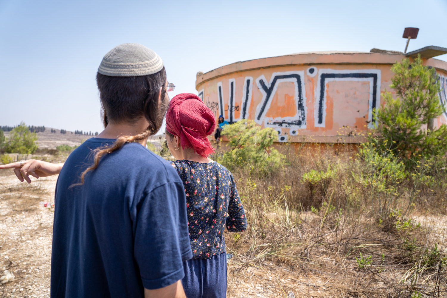 Settlers walk by the water tower on the ruins of the evacuated settlement of Homesh on August 27, 2019. (Hillel Maeir/Flash90)