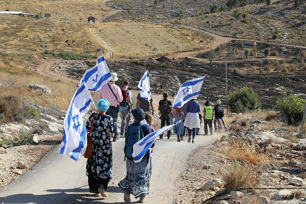 Israeli settlers hold the Israeli flag and signs reading "Preserving and saving the Israeli land" in Bat Ayin and the Gush Etzion junction, June 21, 2021. (Gershon Elinson/Flas90)