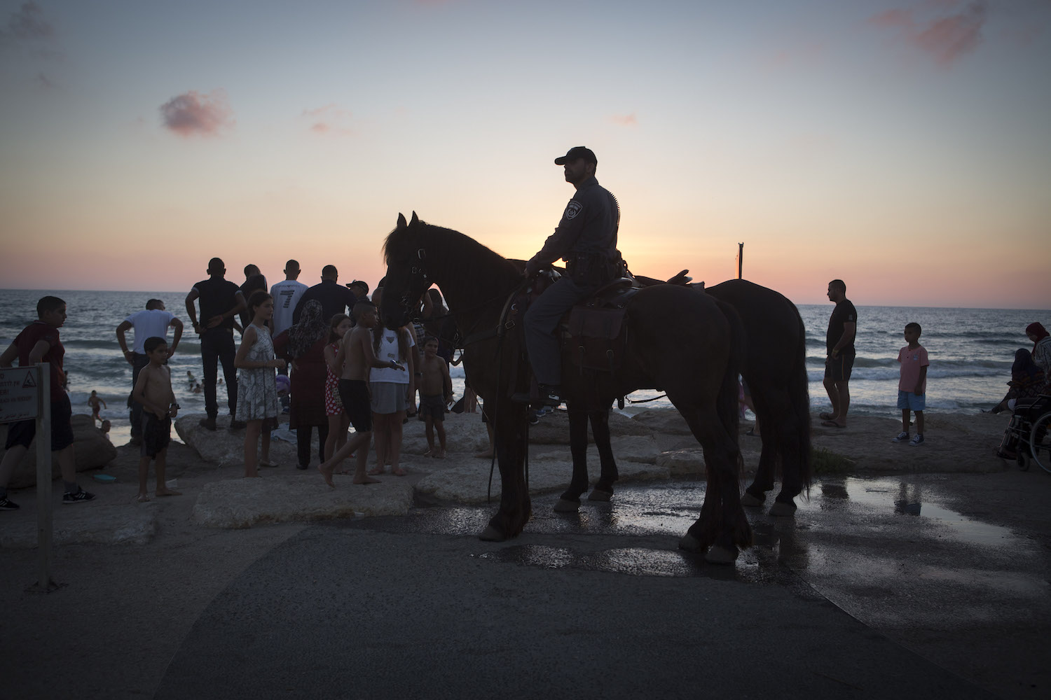A mounted Israeli policeman looks on as Palestinians enjoy an evening on the beach on the border of Tel Aviv and Jaffa during the second day of Eid al-Fitr, July 7, 2016. (Oren Ziv)