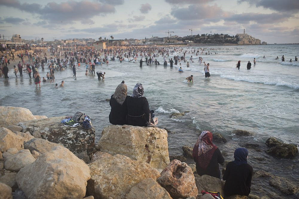 Palestinians, many of whom came from the West Bank, sit near the Mediterranean Sea during the last day of the Eid al-Fitr holiday as the sun sets in Jaffa, July 19, 2015. (Oren Ziv)