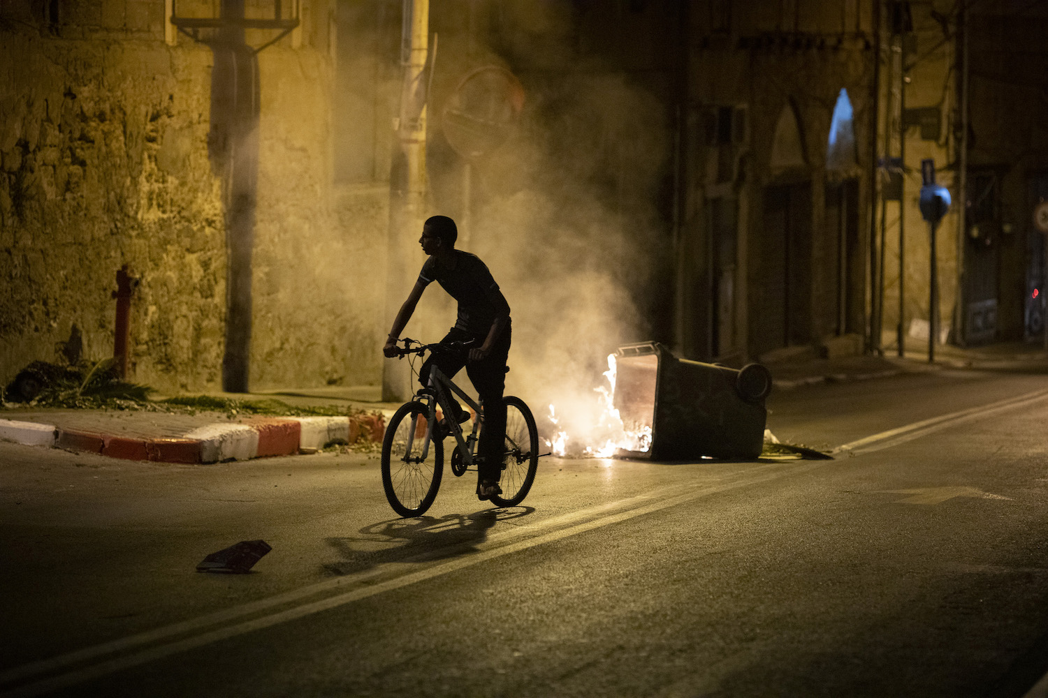 A young Palestinian rides his bike in Jaffa as Israeli police disperse Palestinians protesting against the Tel Aviv municipality's plan to build a homeless shelter and commercial space over an 18th-century Muslim cemetery, July 18, 2020. (Oren Ziv)