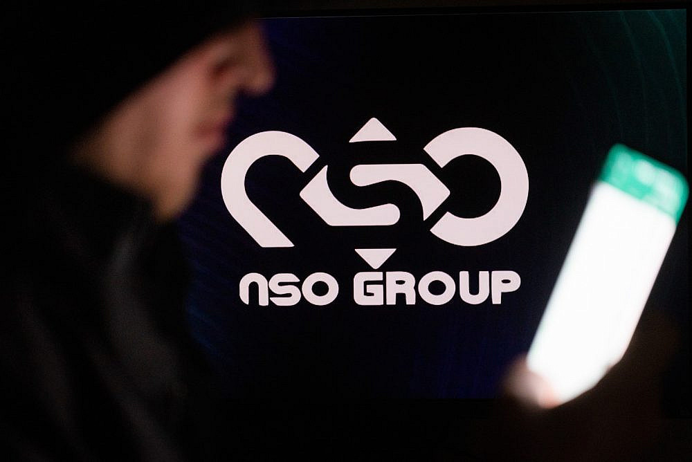 Illustrative photo of a man holding his phone with NSO Group logo, February 7, 2022. (Yonatan Sindel/Flash90)
