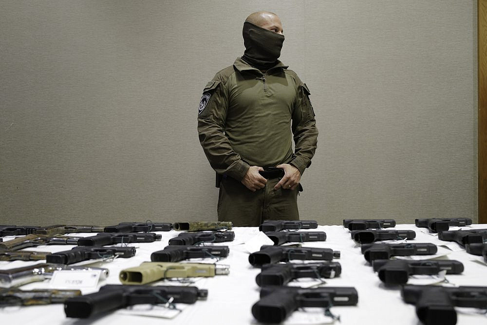 An Israeli police officer seen looking over a display of confiscated illegal weapons during a ceremony following the largest ever police operation against illegal gun dealers, Nazareth, November 9, 2021. (Michael Giladi/Flash90)