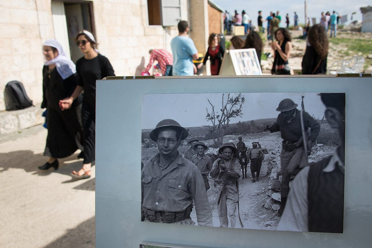 Palestinian citizens of Israel in the destroyed village of Iqrit walk by a historic photograph showing the displacement of the village by the Israeli military during the Nakba, April 21, 2014. (Ryan Rodrick Beiler/Activestills.org)