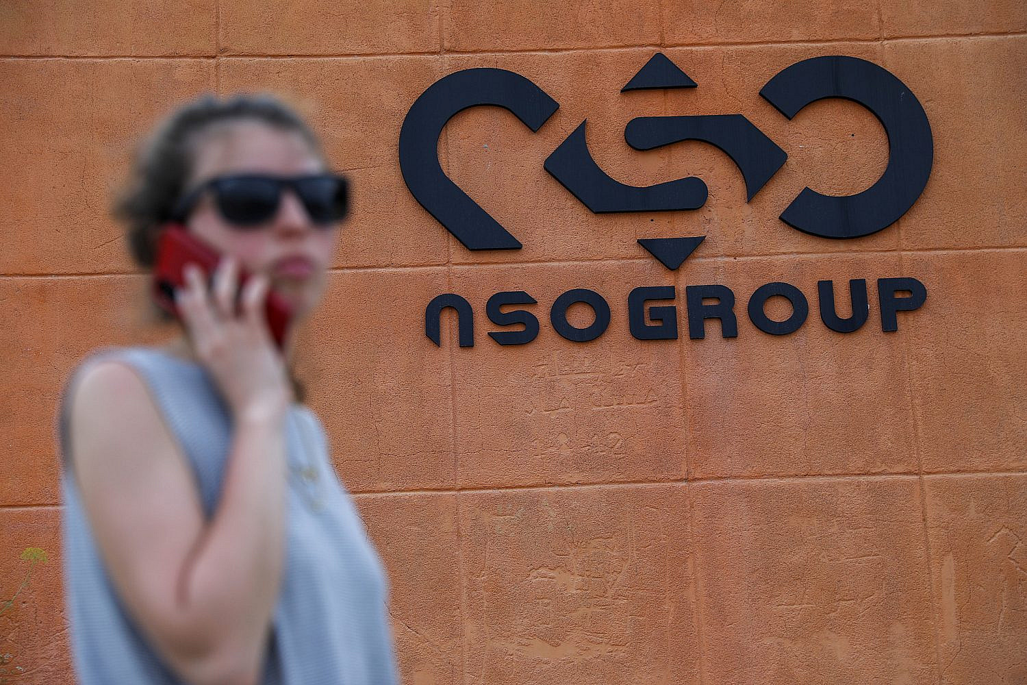 A woman standing with her phone next to the NSO Group company logo, outside the NSO Group offices in Sapir, southern Israel, April 2, 2022. (Noam Revkin Fenton/Flash90)