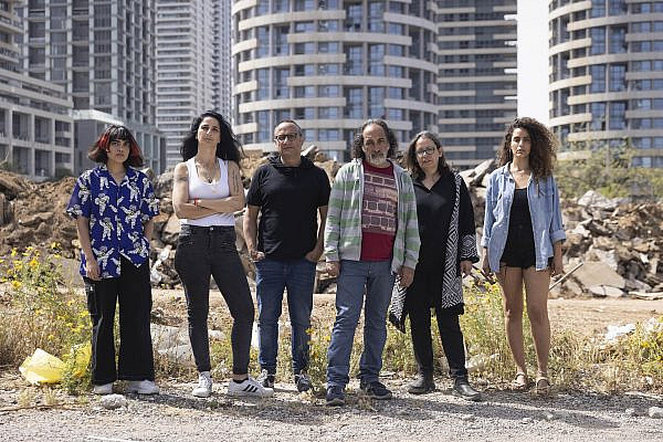 Activists from the Shovrot Kirot movement stand in front of the ruins of the Givat Amal neighborhood in north Tel Aviv, and the luxury apartment blocks built in its place, April 11, 2022. (Oren Ziv)