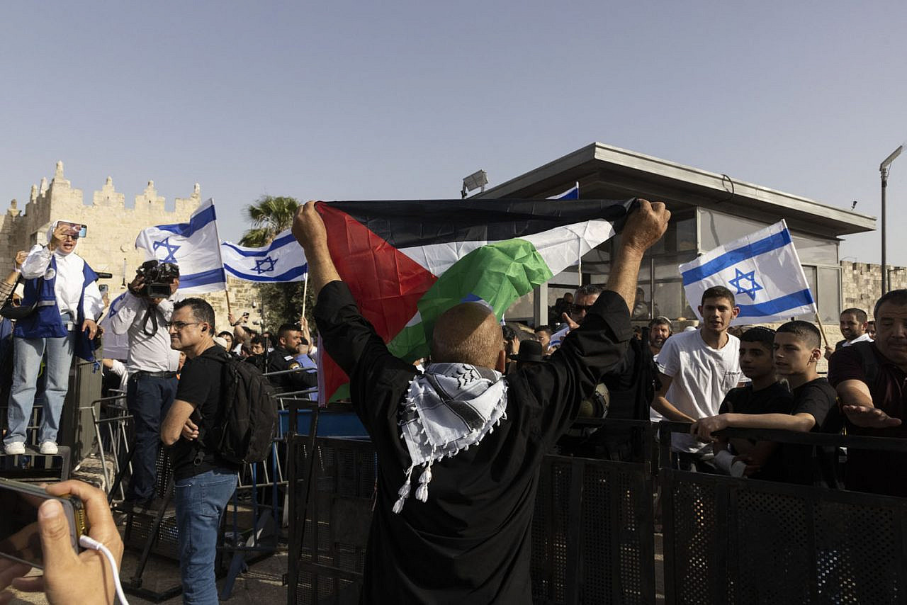 A Palestinian demonstrator holds up a Palestinian flag in front of the Flag March procession, moments before police arrested him, May 29, 2022. (Oren Ziv)