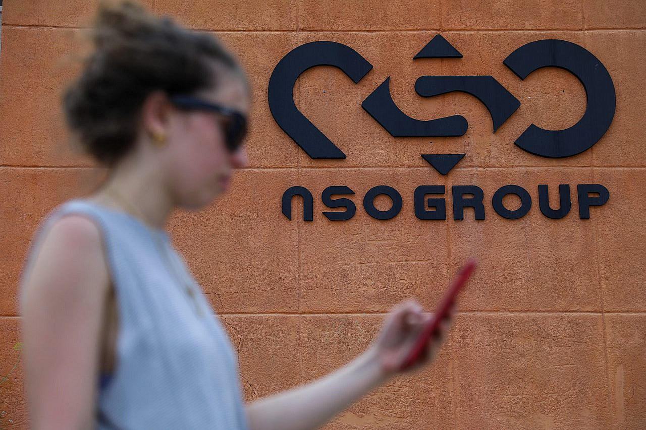 A woman standing with her phone next to the NSO Group company logo, outside the NSO Group offices in Sapir, southern Israel, April 2, 2022. (Noam Revkin Fenton/Flash90)
