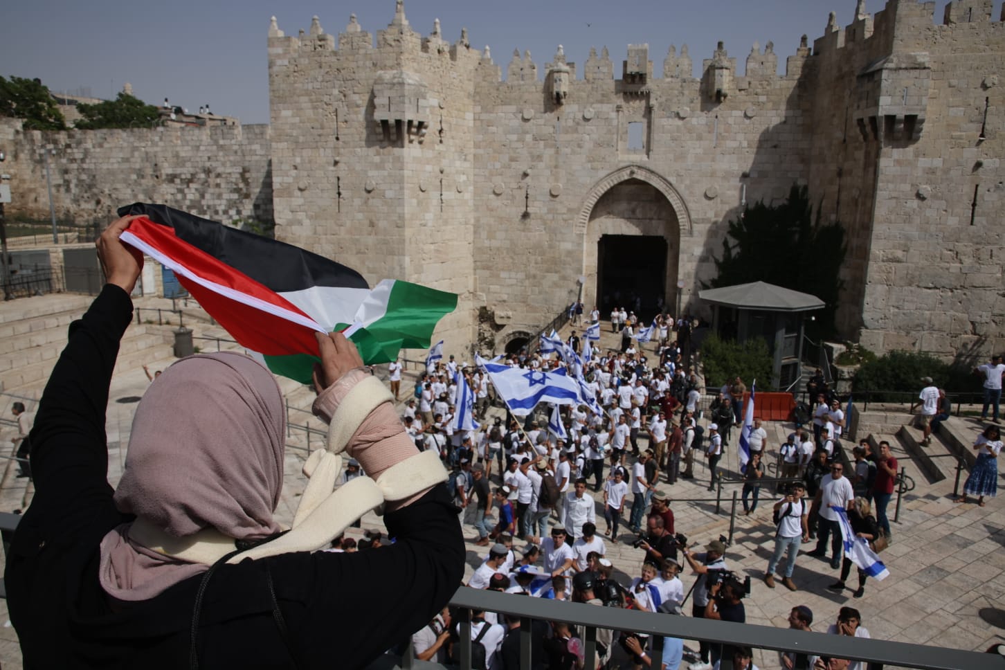 A Palestinian woman waves a flag in front of the Israeli Flag March on Jerusalem Day at Damascus Gate, Jerusalem, May 29, 2022. (Oren Ziv)