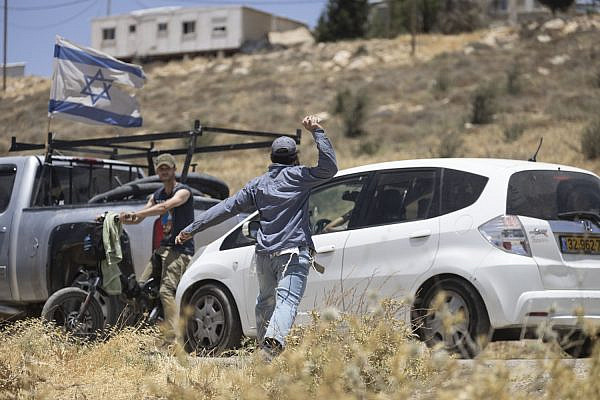 An Israeli settler throws a stone at the window of a car containing three left-wing Israeli activists, as another settler blocks their exit, outside the Mitzpe Yair outpost, occupied West Bank, June 10, 2022. (Oren Ziv)