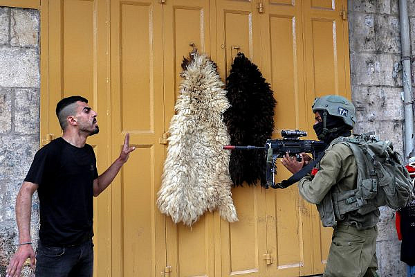 An Israeli soldier points his weapon at a Palestinian man during a protest in Hebron, occupied West Bank, April 22, 2022. (Wisam Hashlamoun/Flash90)