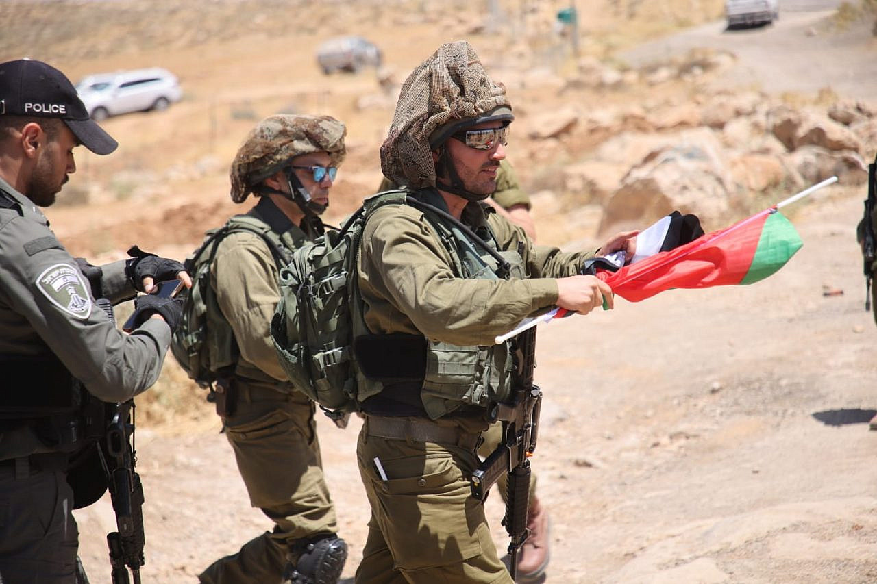 An Israeli soldier confiscates a Palestinian flag carried by a protester at a demonstration against the expulsion of Palestinian communities from what Israel calls Firing Zone 918, Masafer Yatta, occupied West Bank, June 10, 2022. (Oren Ziv)