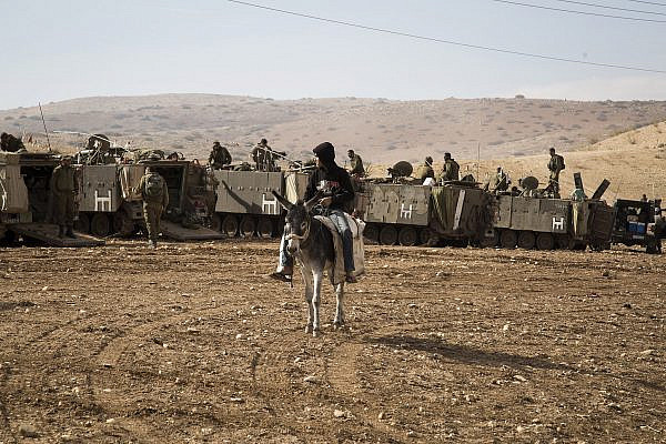 A Palestinian boy on a donkey looks at Israeli army vehicles as they park during an Israeli military training in the northern Jordan valley, West Bank, on December 8, 2016. (Keren Manor/Activestills)