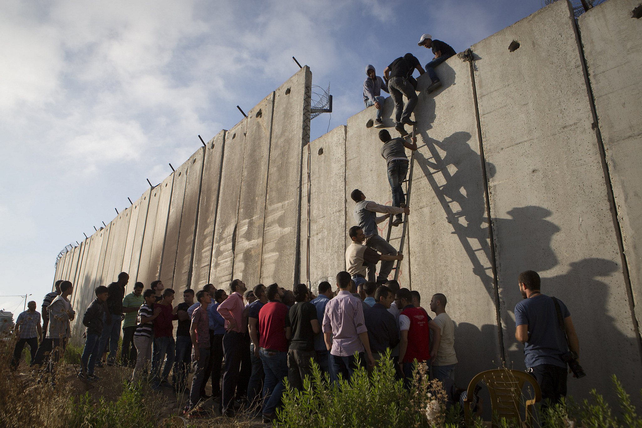Palestinians climb over the Israeli Separation Wall to attend the Friday prayer in Al-Aqsa Mosque, in the town of Al-Ram, West Bank, during the Muslim holy month of Ramadan, July 3, 2015. (Oren Ziv/Activestills)