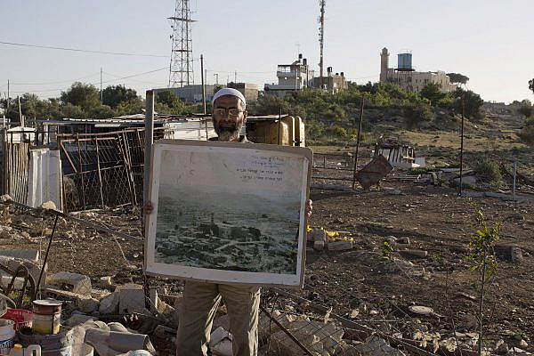 A Palestinian resident of An-Nabi Samwil, occupied West Bank, stands in front of the Tomb of Samuel, holding an old photo showing how the village looked before Israel demolished the Palestinians' houses in the vicinity in order to displace the residents and build a new luxury Jewish settlement, April 28, 2014. (Keren Manor/Activestills)
