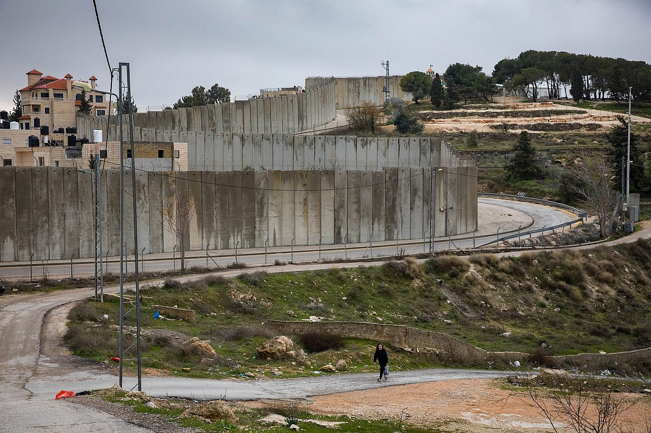 Palestinians walk past a section of the separation wall in the East Jerusalem village of Abu Dis, February 2, 2020. (Olivier Fitoussi/Flash90)