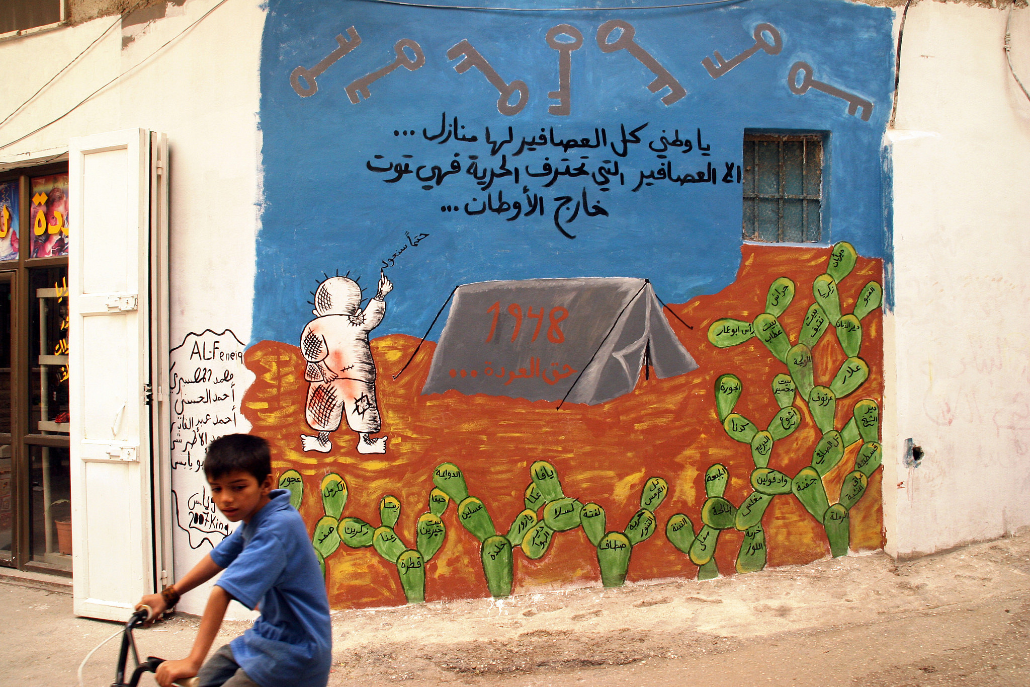 A Palestinian child passes by with his bicycle in front of a mural symbolizing the refugees plight, in Dheisheh refugee camp, in the West Bank city of Bethlehem, May 10, 2007. (Anne Paq/Activestills)