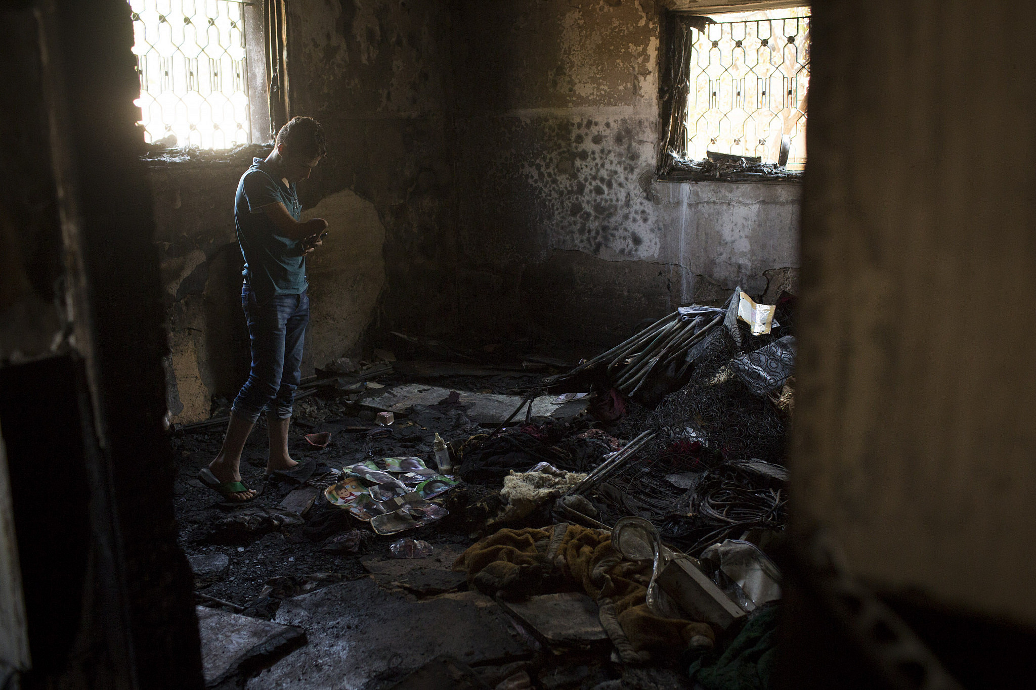 A Palestinian man look at the damaged house of the Dawabsheh family, which was set on fire by Jewish settlers and where 18-month-old toddler Ali died, in the West Bank village of Duma, July 31, 2015. (Oren Ziv/Activestills)