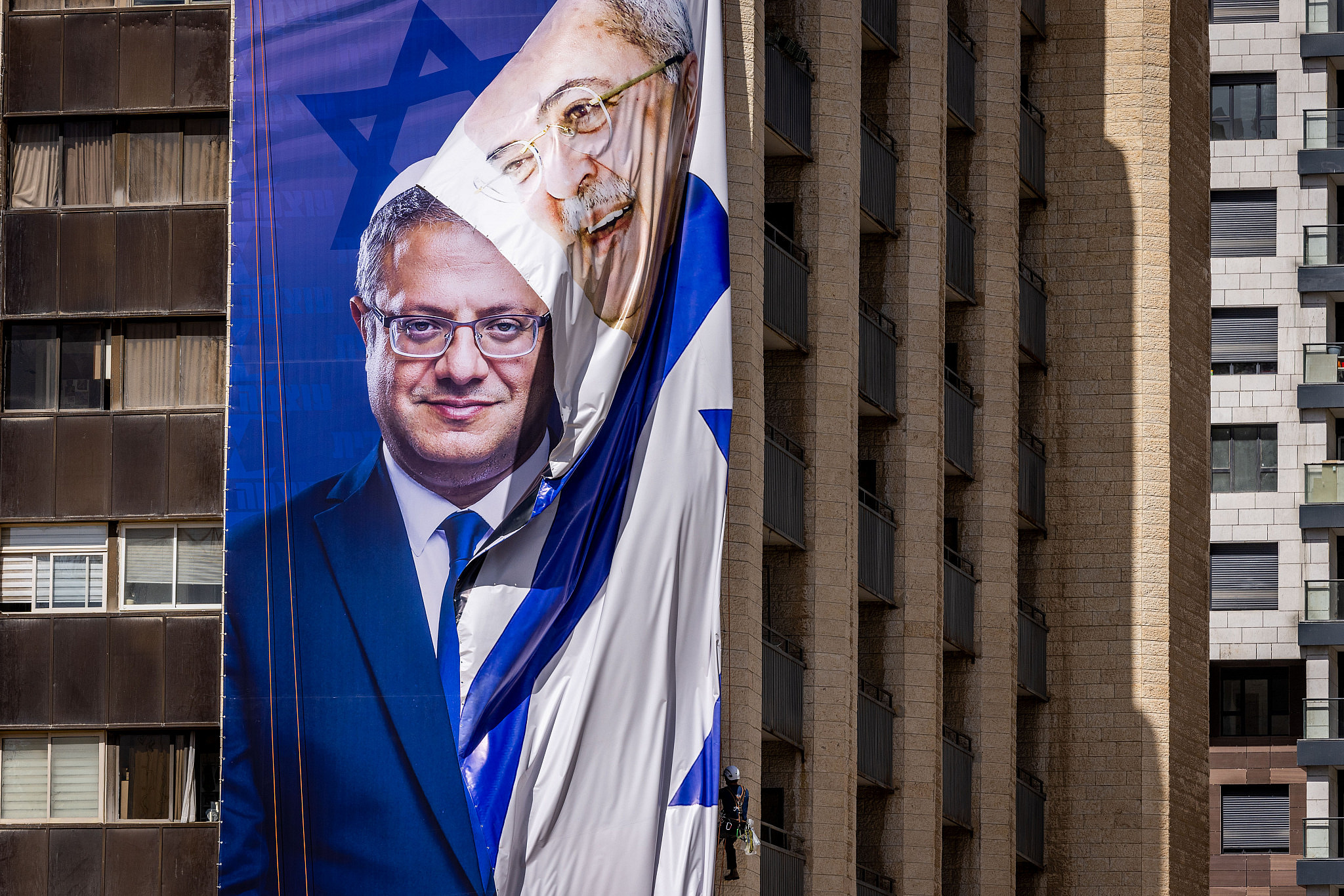 Workers hang a large election campaign poster of Otzma Yehudit head Itamar Ben Gvir and take down a poster of Arab MK Ahmad Tibi, in Jerusalem on September 29, 2022. (Yonatan Sindel/Flash90)