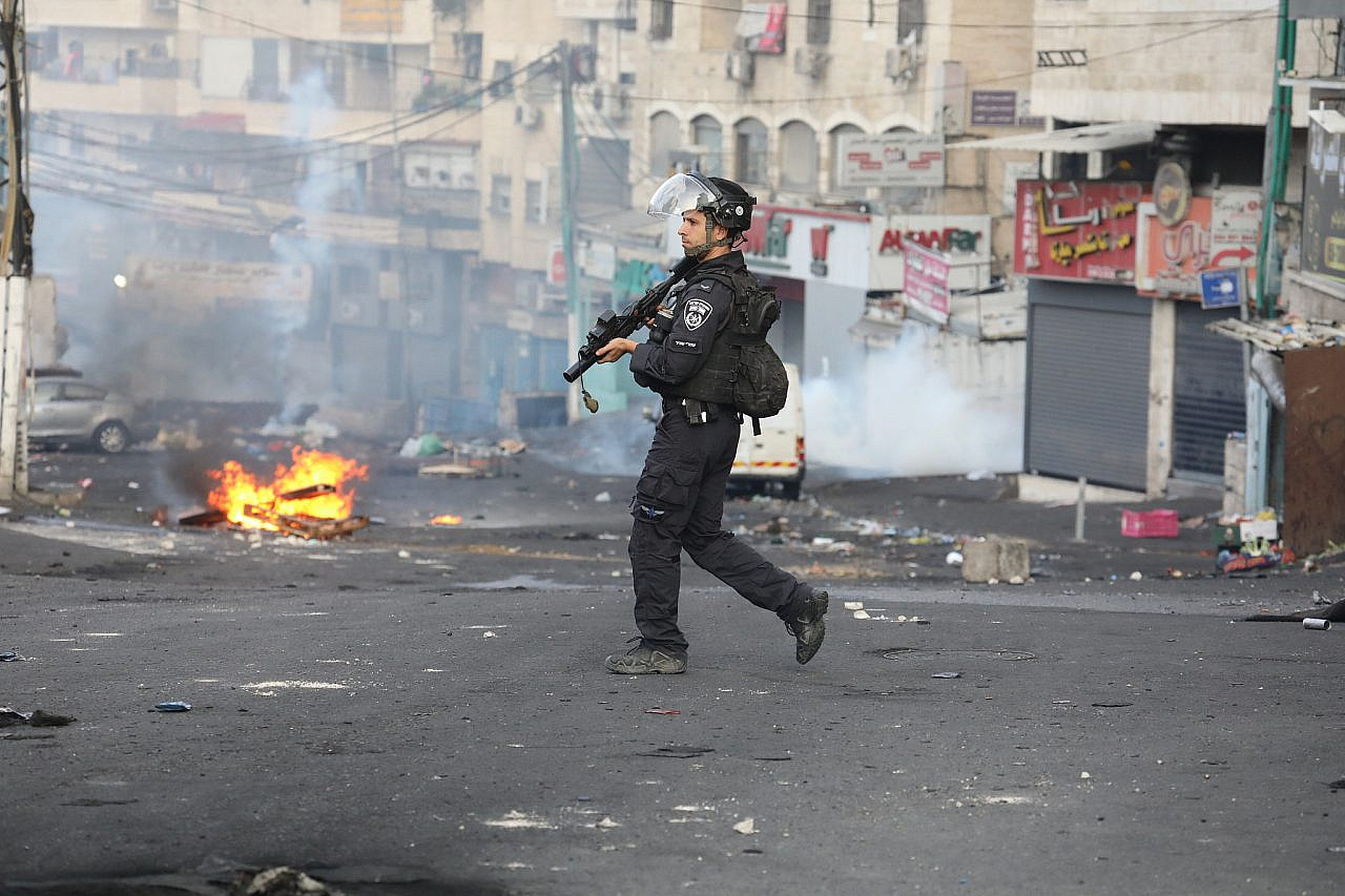 An Israeli police officer in front of shuttered shops during a day of civil disobedience in Shuafat Refugee Camp, October 12, 2022. (Oren Ziv/Activestills)