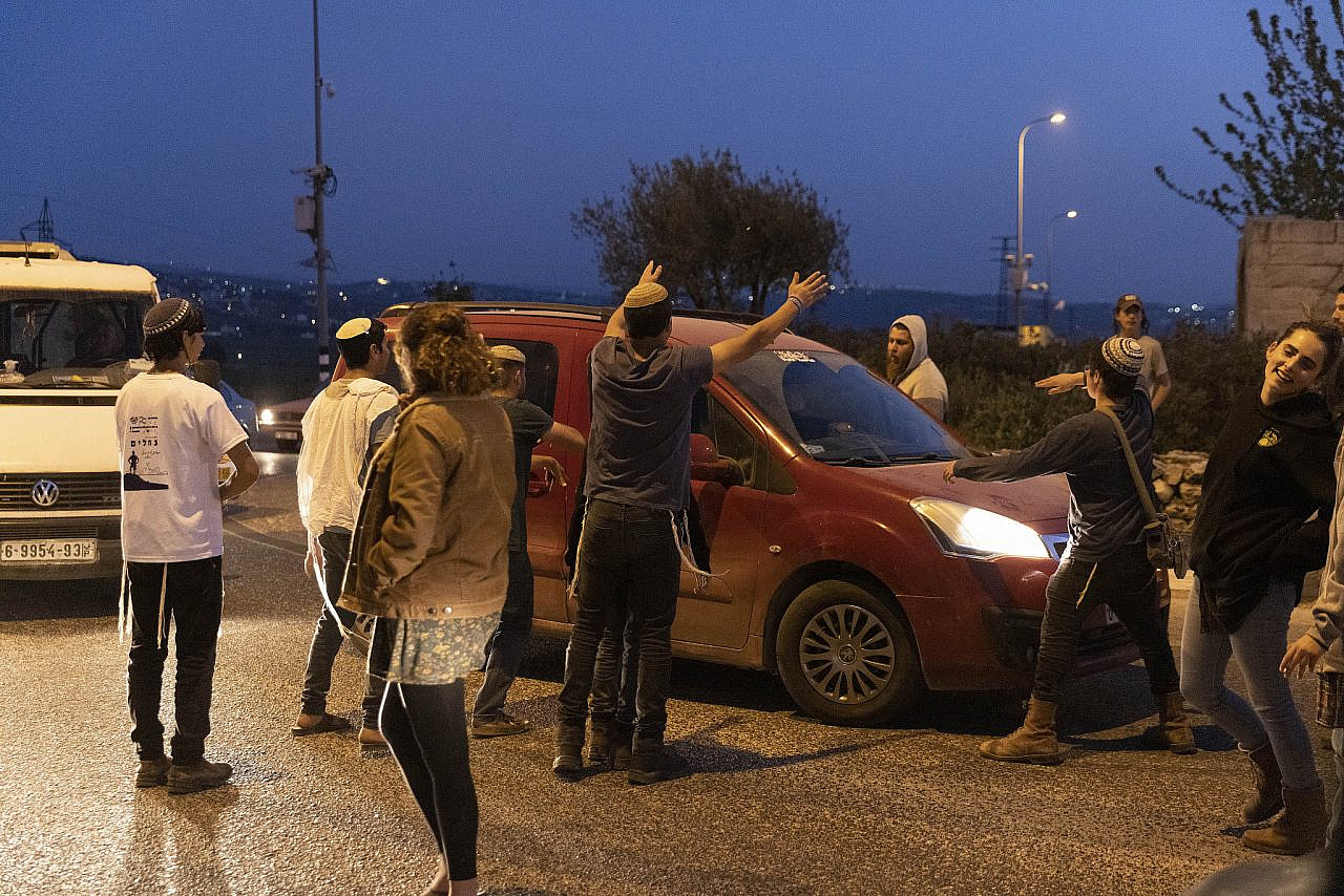 Israeli settlers block a main road outside Nablus, occupied West Bank, and attack Palestinian vehicles while the Israeli army closes several military gates to Palestinian areas and turns back Palestinian traffic, April 10, 2022. (Oren Ziv)