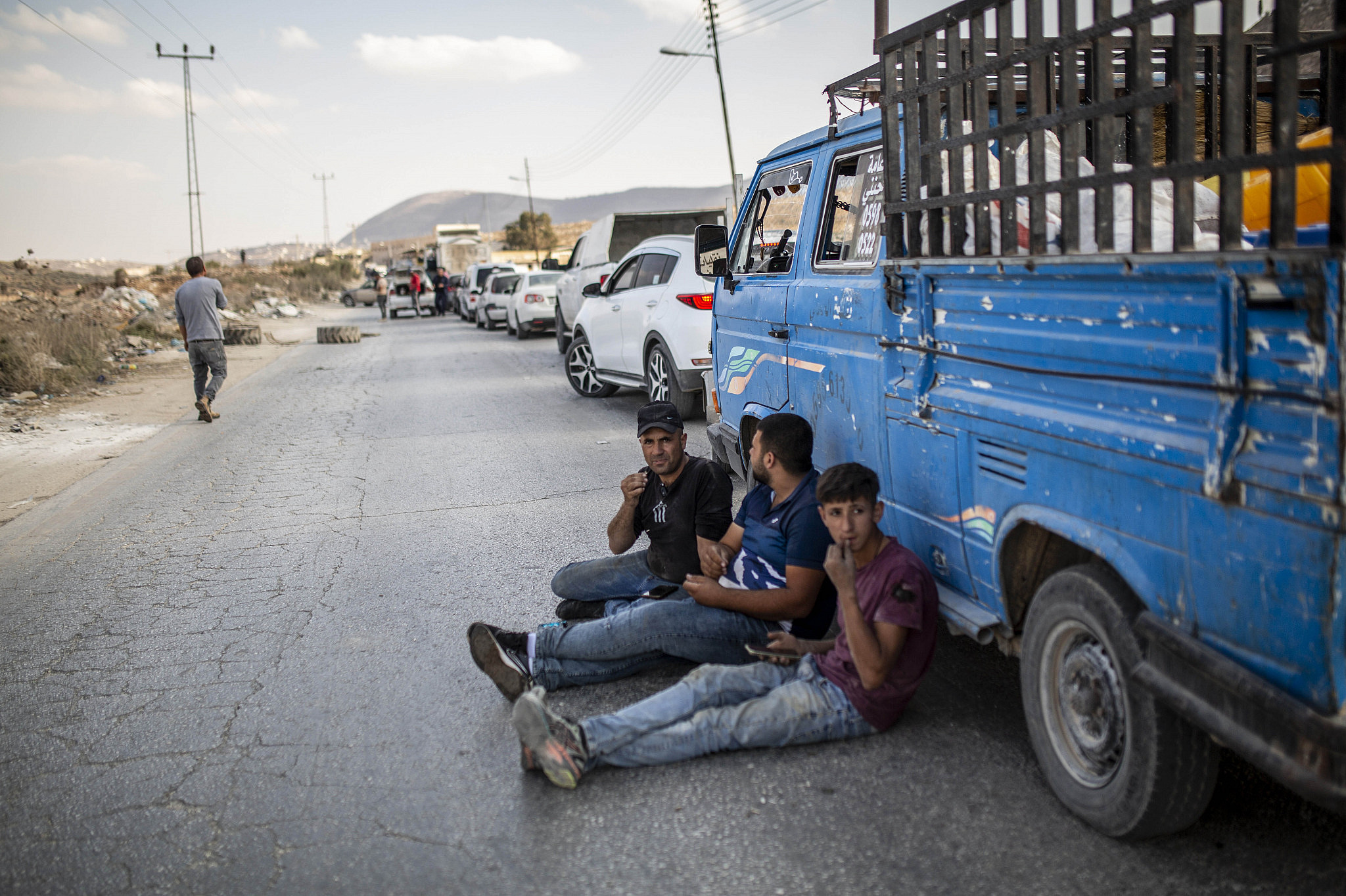 Palestinians sit on the road while waiting to pass through the Israeli military checkpoint in the village of Beit Furik, near Nablus, occupied West Bank, October 20, 2022. (Anne Paq/Activestills)