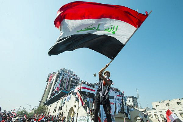 An Iraqi protester waves a flag at a protest during the October Revolution, November 1, 2019. (Mondalawy/CC BY-SA 4.0)