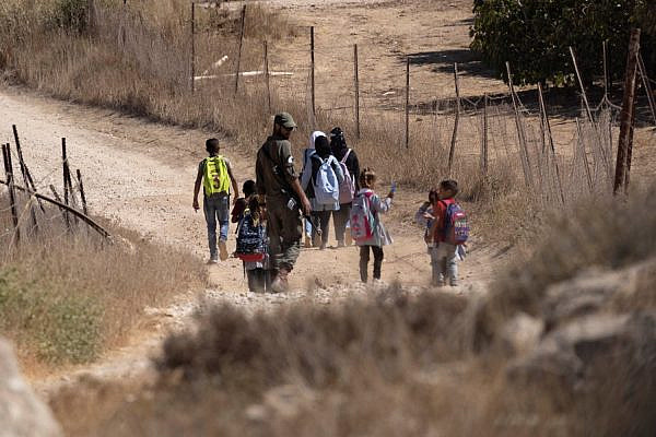 Israeli soldiers accompany Palestinian students heading back home to the village of Tuba, at the end of their school day in the village of A-Tuwani, as they walk on a two-kilometer dirt road by the Israeli settlement of Maon, West Bank, September 28, 2021. (Oren Ziv)