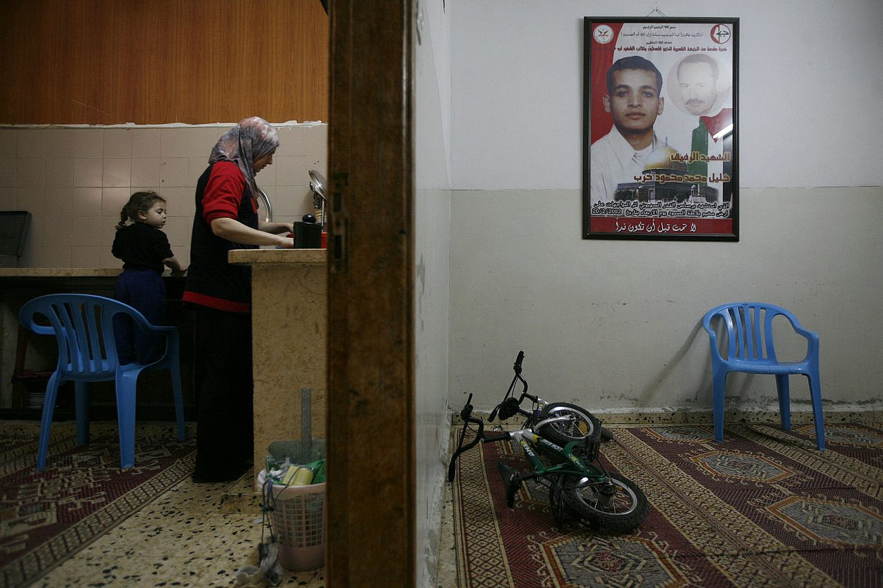 A photograph depicting a young Palestinian man killed during the Second Intifada hangs on the wall of a house in the Balata Refugee Camp, where a mother and her daughter prepare food, April 18, 2009. (Miriam Alster/Flash90)